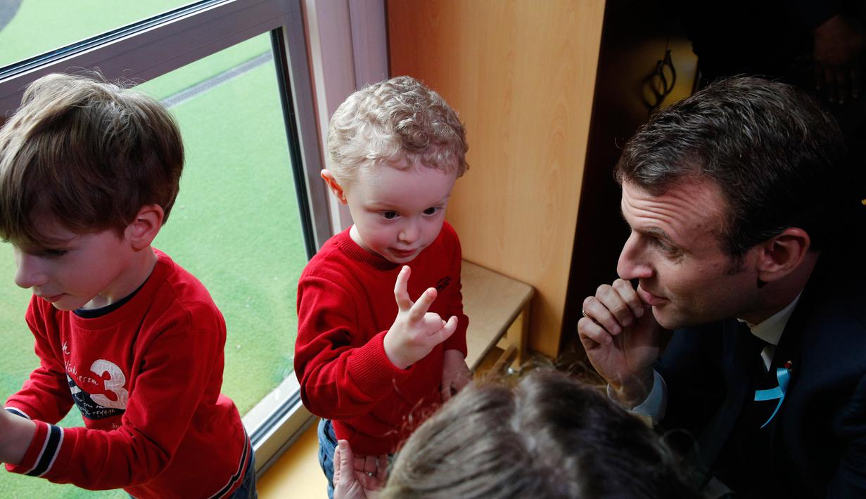 Presiden Prancis Emmanuel Macron menyimak pembicaraan anak-anak saat mengunjungi Graffiti's- Association Le Moulin Vert di Normandia, Prancis (5/4). (AP / Christophe Ena, Pool)