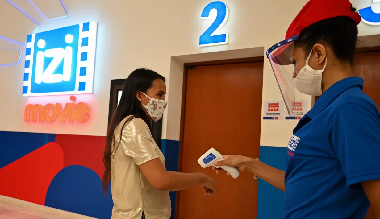 Seorang petugas mengukur suhu pengunjung sebelum memasuki bioskop yang dibuka kembali menyusul pelonggaran langkah-langkah yang diberlakukan oleh pemerintah Kolombia untuk menghentikan penyebaran Covid-19, di Cali, Kolombia pada Jumat (2/10/2020). (Photo by Luis ROBAYO / AFP)