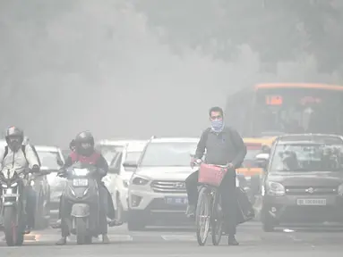 Seorang pengendara sepeda dengan wajah ditutupi masker melintasi sebuah jalan di pagi hari yang dingin dan berkabut di New Delhi pada tanggal 18 November 2024. (Money SHARMA/AFP)