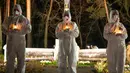 Orang-orang yang mengenakan pakaian pelindung putih memegang lilin selama upacara peringatan yang didedikasikan untuk petugas pemadam kebakaran dan pekerja yang meninggal setelah bencana nuklir Chernobyl, menjelang peringatan 40 tahunnya di Slavutych, Ukraina, Sabtu, 25 April 2026. (AP Photo/Dan Bashakov)