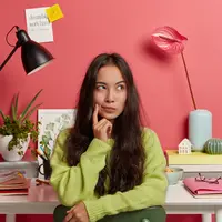 Seorang perempuan berambut panjang sedang berpikir dengan memegang pipinya menggunakan telunjuk (Foto Dok: Freepik/wayhomestudio).