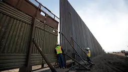 Pekerja melihat di antara pagar perbatasan Amerika Serikat (AS) dengan Meksiko di Calexico, California, AS, Minggu (5/3). Pembangunan tembok pembatas di area ini sudah direncanakan sejak zaman Barack Obama tahun 2009. (AP Photo/Gregory Bull)