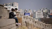 Suami istri melihat ponsel mereka ketika mereka duduk di lereng bukit yang menghadap ke cakrawala kota di Seoul, Korea Selatan (2/4). Korea Selatan sedang bersiap untuk meluncurkan jaringan seluler 5G pertama di dunia pada 5 April. (AFP Photo/Ed Jones)