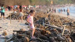 Seorang gadis melintas di atas sampah yang terdampar akibat cuaca buruk di Pantai Kuta, Bali, Jumat (15/2). Sampah bervolume besar kembali menepi di Pantai Kuta, kali ini pesisir pantai berpasir putih itu dipenuhi sampah buah kelapa. (SONNY TUMBELAKA/AFP)