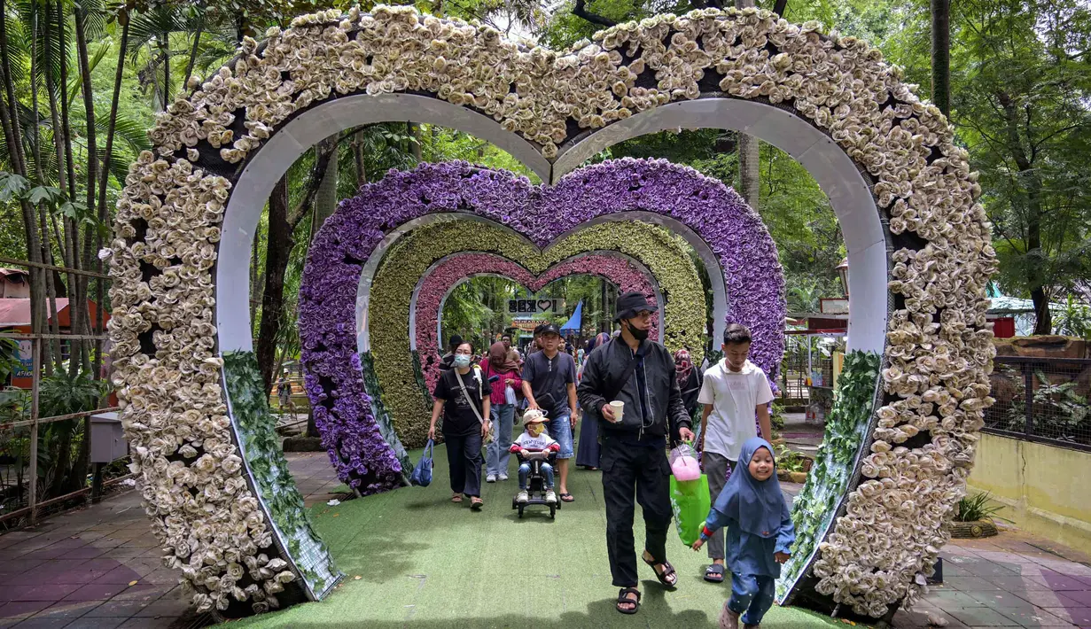 Meski peningkatan jumlah kunjungan sempat melambat akibat cuaca hujan, namun secara keseluruhan, pengelola Kebun Binatang Surabaya (KBS) menargetkan kenaikan jumlah pengunjung sebesar 10-15 persen selama periode libur sekolah dan Nataru 2025. Tampak dalam foto, pengunjung berjalan melewati dekorasi berbentuk hati di Kebun Binatang Surabaya, Jawa Timur, selama libur sekolah sekaligus jelang Natal dan Tahun Baru pada Minggu 21 Desember 2025. (JUNI KRISWANTO/AFP)