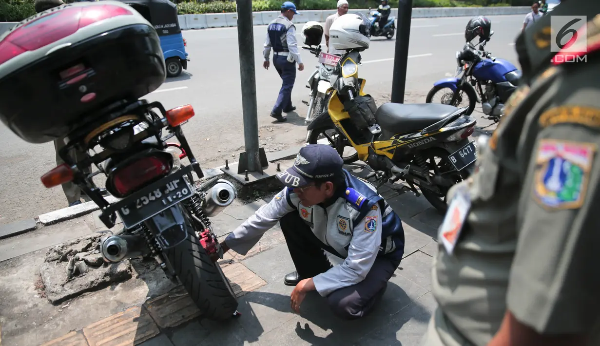 Petugas Dishub DKI menggembosi ban motor yang nekat parkir liar di trotoar sepanjang Jalan Kramat Raya, Senen, Jakarta, Jumat (22/9). Razia dilakukan untuk mengantisipasi arus lalu lintas yang kerap macet di kawasan itu. (Liputan6.com/Faizal Fanani)