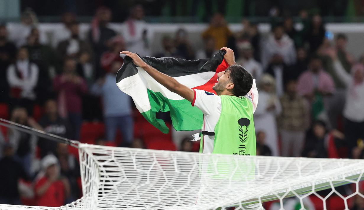 Pemain Yordania, Yazan Al-Naimat membentangkan bendera negaranya saat merayakan kemenangan timnya atas Korea Selatan setelah laga semifnial Piala Asia 2023 di Ahmad Bin Ali Stadium, Doha, Qatar, Selasa (06/02/2024). (AFP/Giuseppe Cacace)