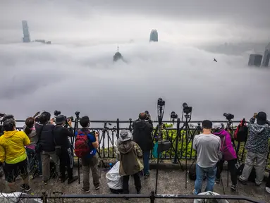 Orang-orang mengambil foto kabut di atas Hong Kong, Selasa (22/3/2022). Kabut tebal menyelimuti Hong Kong pada musim semi ketika wilayah tersebut dipengaruhi oleh udara dingin dan hangat bergantian. (AFP/Dale De La Rey)