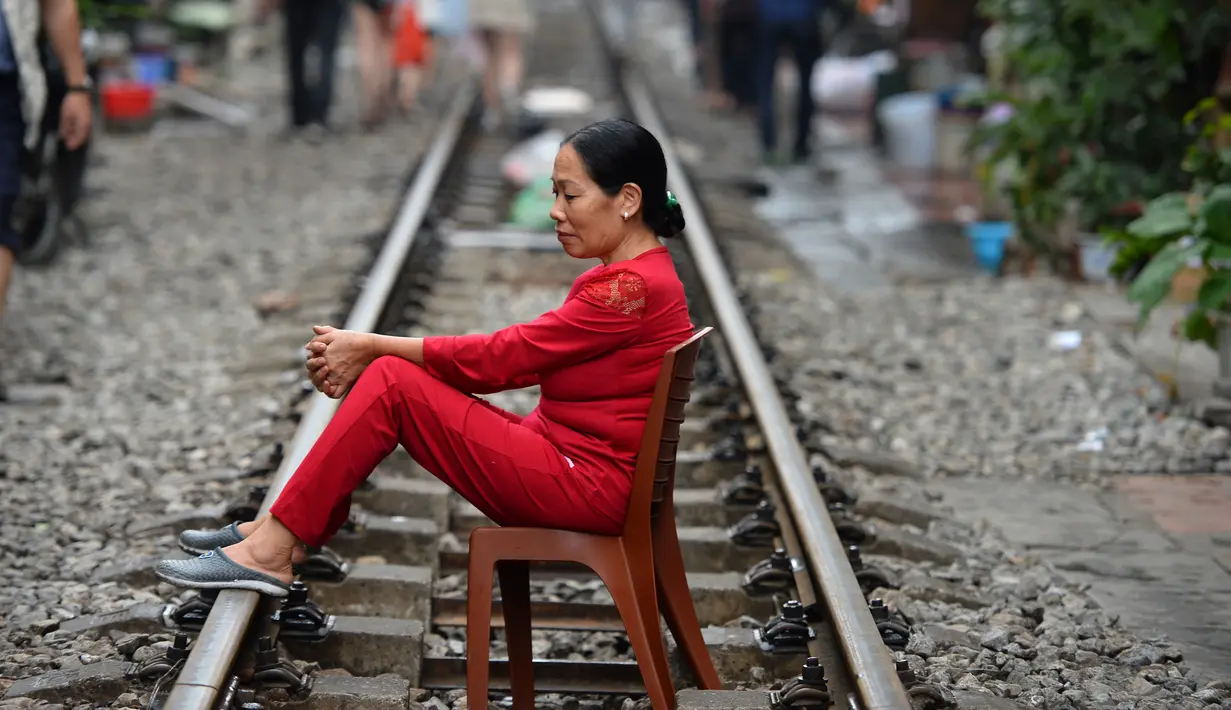 Seorang wanita Vietnam duduk di atas kursi di tengah jalur kereta api yang melintasi kawasan permukiman di Hanoi, 20 Oktober 2018. Rel kereta ini menjadi titik bagi wisatawan untuk berfoto dan mengunggahnya di jejaring sosial. (Nhac NGUYEN/AFP)