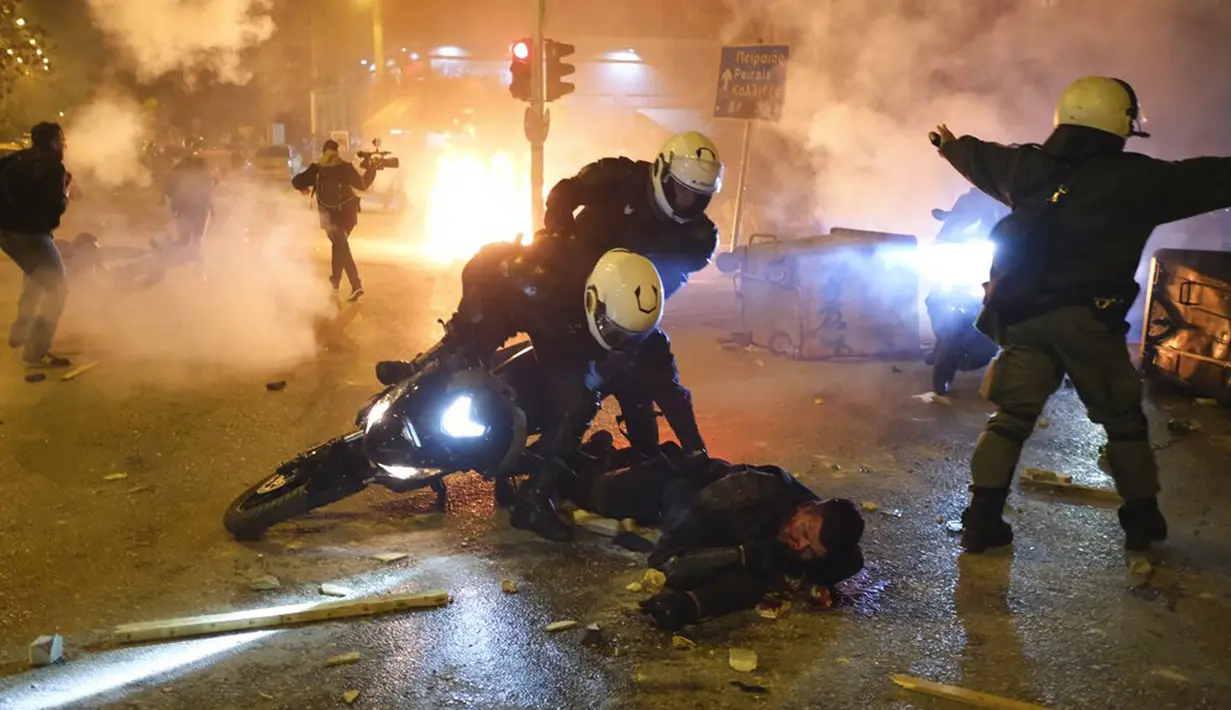 Seorang polisi terluka dalam bentrokan dengan pengunjuk rasa ketika rekan-rekannya mencoba membantunya, Athena, Yunani, Selasa (9/3/2021). Bentrokan parah terjadi di Athena setelah pemuda yang memprotes insiden kekerasan polisi menyerang kantor polisi dengan bom bensin. (AP Photo/Aggelos Barai)