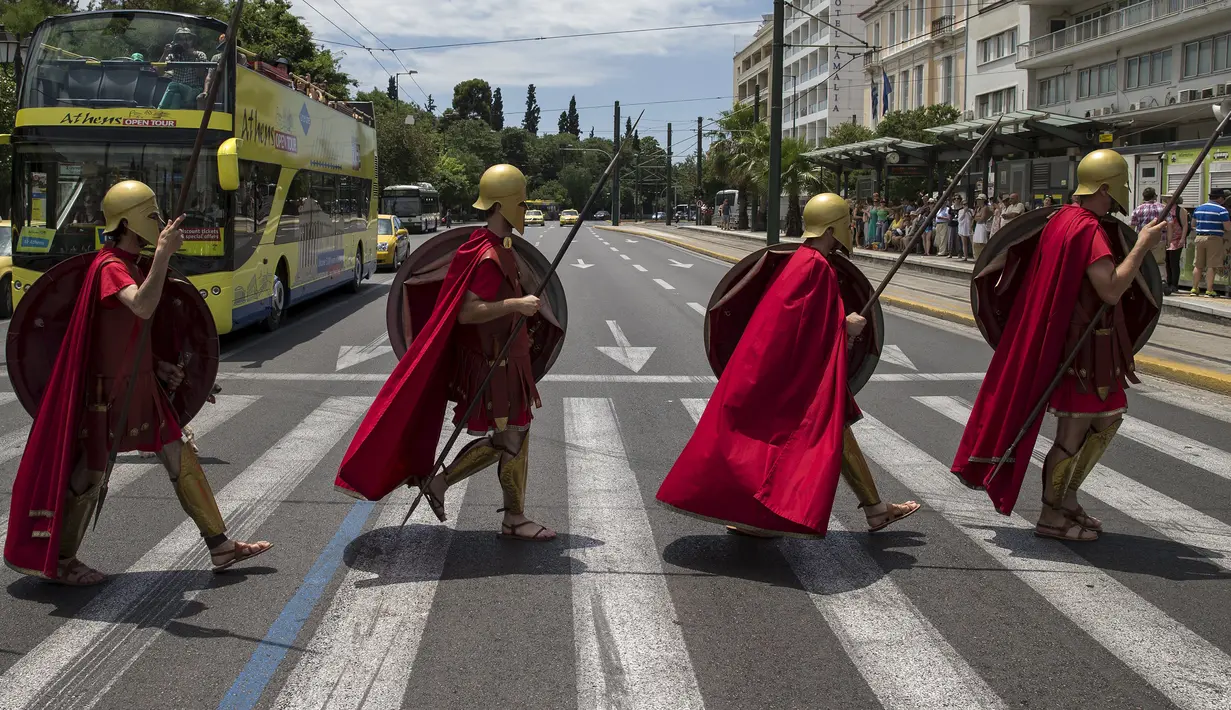 Sekelompok Pria berpakaian seperti tentara Yunani kuno menyeberang jalan sambil membawa tombak, perisai saat pertunjukan di Konstitusi (Syntagma) persegi di Athena, Yunani (21/6/2015). (REUTERS /Marko Djurica)