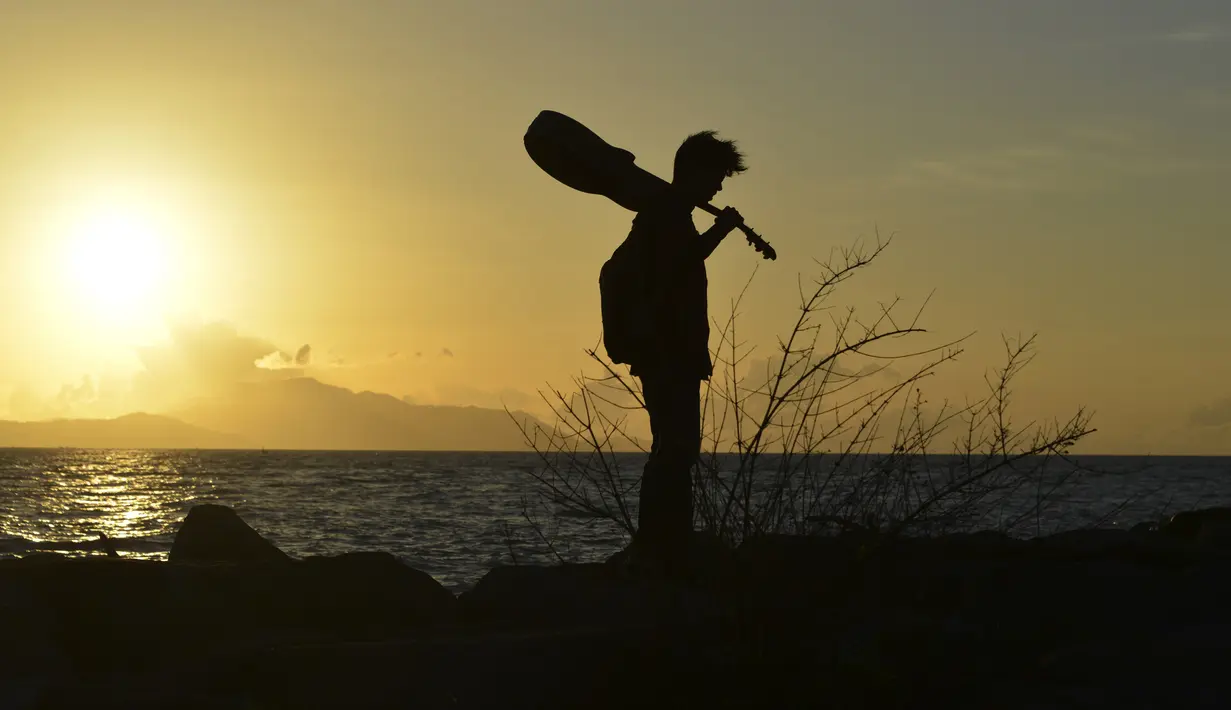 Seorang pria membawa gitar sambil menyusuri pantai saat matahari terbenam di Banda Aceh pada 28 Juni 2019. Pemandangan makin sempurna saat matahari tenggelam hingga alam berubah semakin remang dan romantis. (Photo by CHAIDEER MAHYUDDIN / AFP)