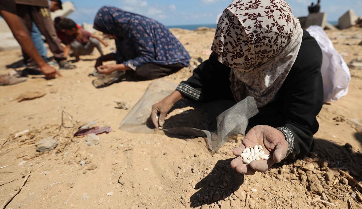 Perserikatan Bangsa-Bangsa (PBB) memperingatkan bahwa Gaza kini menghadapi bencana kelaparan dan kehancuran total. Tampak dalam foto, para perempuan Palestina mencari kacang-kacangan atau beras di pasir di Nuseirat, Jalur Gaza tengah, pada 5 Agustus 2025. (Eyad BABA/AFP)