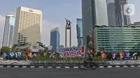 Pengendara sepeda motor melintas di dekat maskot Pekan Olahraga Nasional (PON) XX Papua di Bundaran Hotel Indonesia, Jakarta, Jumat (16/07/2021). Pemasangan maskot PON XX Papua itu bentuk promosi kegiatan pekan olahraga yang diselenggarakan tiap empat tahun sekali. (Liputan6.com/Herman Zakharia)