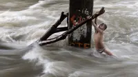 Seorang bocah laki-laki memegang batang pohon saat ia bermain di sungai dengan arus yang sangat deras akibat hujan lebat di bawah jembatan di Manila, Filipina (11/6). (AFP Photo/Noel Celis)