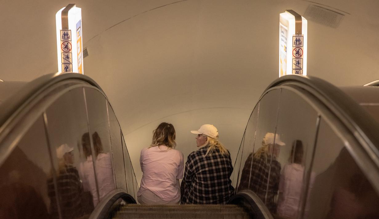Para perempuan duduk di eskalator saat mereka berlindung di stasiun metro Teatralna selama alarm serangan udara di ibu kota Ukraina, Kyiv, pada 26 Juli 2023, di tengah invasi Rusia ke Ukraina. (Roman PILIPEY / AFP)