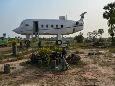 Foto yang diambil pada 12 Maret 2023 ini memperlihatkan Chrach Peou sedang menyemprotkan air di taman depan rumahnya yang berbentuk pesawat terbang di provinsi Siem Reap, Kamboja. (Photo by TANG CHHIN SOTHY / AFP)