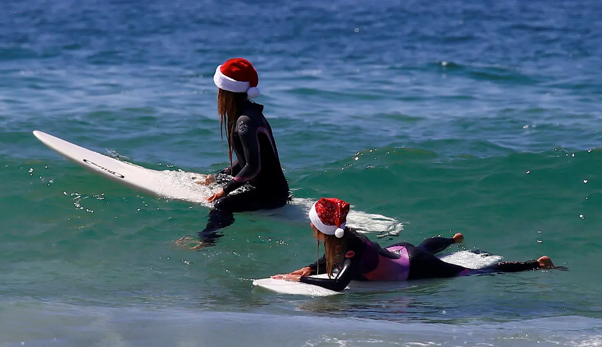 Dua wisatawan asal Jerman mengenakan topi Natal bersiap bermain surfing di Bondi Beach Sydney pada Hari Natal di Australia, (25/12). (REUTERS/David Gray)