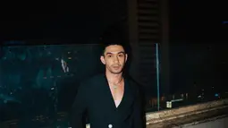 Dalam foto, Reza Rahadian mengenakan blazer hitam dengan belahan dada membentuk huruf V yang dipadu dengan celana panjang hitam tanpa motif dan sepatu pantovel hitam mengilap. Agar tak monoton, ia pakai kalung perak. Bros serupa bunga mekar disematkan di sisi kanan perut, plus cincin perak di jari. Kontras dengan warna baju namun justru menghadirkan efek “menyala.” (Foto: Dok. Instagram @hagaipakan)