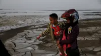 Seorang wanita menggendong anaknya saat mereka berdiri di atas lumpur kering Lapindo di Sidoarjo, Jawa Timur, 11 Oktober 2015. Beberapa tahun silam, Porong didera bencana, namun kini kawasan tersebut malah jadi objek wisata tak biasa. (REUTERS/Beawiharta)