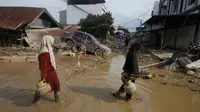 Hingga Kamis (5/12/2025) malam, listrik belum menyala, sehingga jalanan masih gelap gulita. Tampak dalam foto, para penyintas berjalan melewati reruntuhan mobil di area terdampak banjir bandang di Aceh Tamiang, Sumatera, Indonesia, Kamis 4 Desember 2025. (AP Photo/Binsar Bakkara)