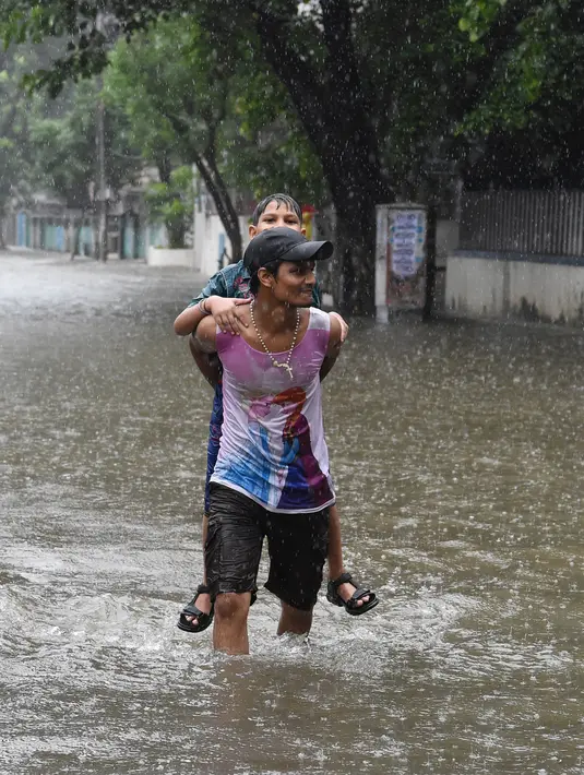 Seorang pria menggendong keluarganya melintasi banjir setelah hujan lebat di Mumbai, India (9/7). Departemen Meteorologi India mengeluarkan peringatan banjir akibat hujan deras di tempat-tempat terpencil di wilayah tersebut. (AFP Photo/Indranil Mukherjee)