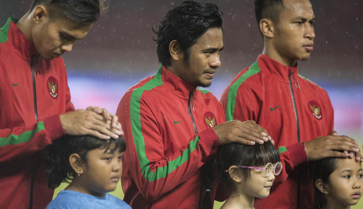 Gelandang Timnas Indonesia, Ilham Udin Armaiyn, melindungi seorang anak dari hujan saat akan melawan Islandia pada laga persahabatan di SUGBK, Jakarta, Minggu (14/1/2018). Timnas Indonesia kalah 1-4 dari Islandia. (Bola.com/Vitalis Yogi Trisna)