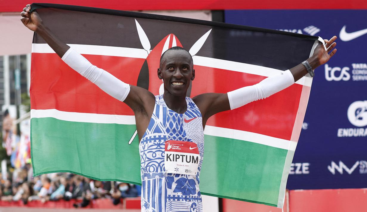 Pelari Kenya, Kelvin Kiptum melakukan selebrasi dengan membentangkan bendera negaranya setelah memenangkan Chicago Marathon 2023 di Chicago, Illinois, Amerika Serikat, 8 Oktober 2023. Ia memecahkan rekor sebagai pelari marathon tercepat di dunia dengan mencatatkan waktu 2 jam 35 detik. (AFP/Kamil Krzaczynski)