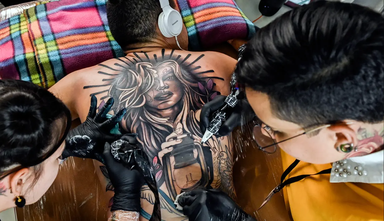 Seniman membuat tato di tubuh seorang pria saat acara Expotattoo Colombia 2019 di Medellin, departemen Antioquia (2/6/2019). Para penggila tato antusias untuk mentato tubuhnya di festival tato terbesar di negara tersebut. (AFP Photo/Joaquim Sarmiento)