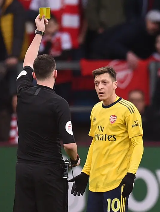 Pemain Arsenal Mesut Ozil (kanan) mendapat kartu kuning dari wasit Chris Kavanagh saat menghadapi Burnley pada pertandingan Liga Inggris di Turf Moor, Burnley, Inggris, Minggu (2/2/2020). Laga berakhir imbang tanpa gol. (Oli SCARFF/AFP)