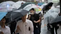 Seorang pria menggunakan payung berjalan saat hujan turun di Tokyo, Jepang (8/8). Sejumlah maskapai membatalkan penerbangan akibat cuaca yang kurang mendukung. (AFP Photo/Behrouz)