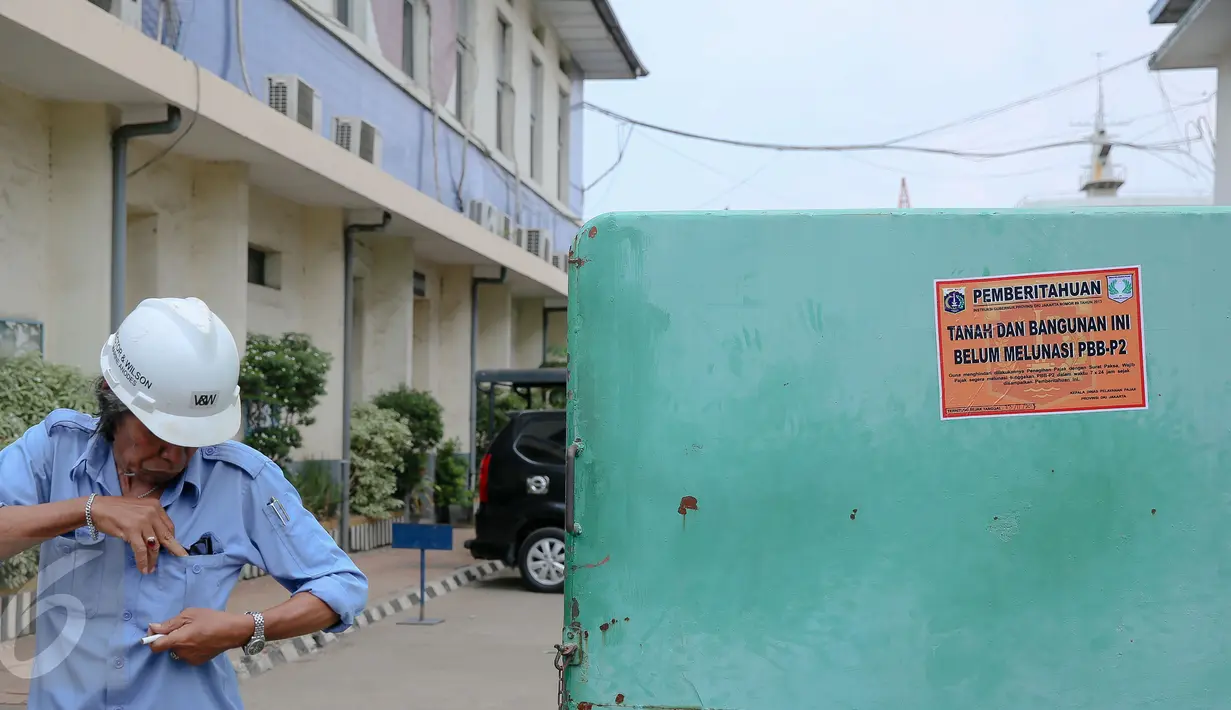 Pekerja berdiri dekat plang yang dipasang  di PT DKB Dok Perkapalan Galangan I, Tanjung Priok, Jakarta, Senin (23/11). Langkah ini sebagai peringatan bagi para wajib pajak (WP) kelas menengah ke atas mencapai ratusan miliar. (Liputan6.com/Faizal Fanani)