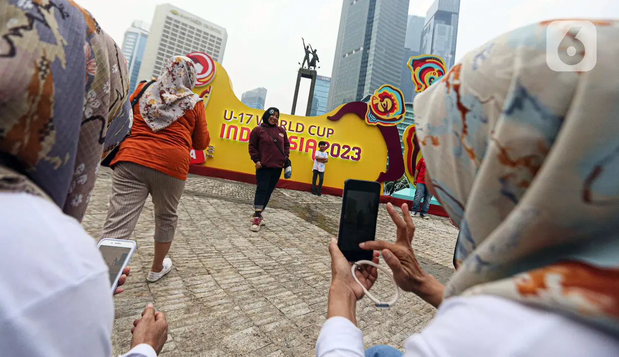 Warga antusias berfoto dengan latar belakang papan promosi Piala Dunia U-17 2023. Mereka pun bergantian untuk berfoto. (Liputan6.com/Faizal Fanani)