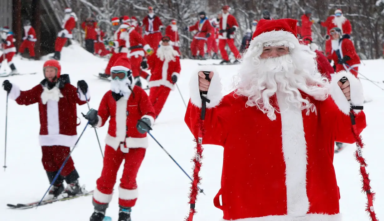 Pemain ski dan snowboarder berpakaian Santa Claus menuruni lereng gunung saat Santa Sunday ke-19 di Newry, Maine, AS, Minggu (2/12). Peserta harus menyumbang 20 US dolar untuk mendukung program pendidikan dan rekreasi setempat. (AP Photo/Robert F. Bukaty)