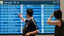 Penumpang melihat papan informasi penerbangan kedatangan di Terminal Internasional Bandara Haneda setelah penerbangan dibatalkan atau ditunda karena badai tropis Jangmi di Tokyo, Jepang, Rabu 3 Juni 2026. (Andrew CAALLERO-REYNOLDS/AFP)
