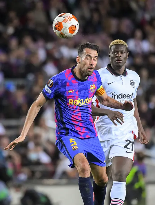 Gelandang Barcelona Sergio Busquets (kiri) dan pemain depan Eintracht Frankfurt Ragnar Ache menyundul bola saat bersaing pada leg 2 perempat final Liga Europa di Camp Nou, Jumat (15/4/2022). Barcelona secara mengejutkan kalah 2-3 dari Eintracht Frankfurt. (Jose Jordan / AFP)