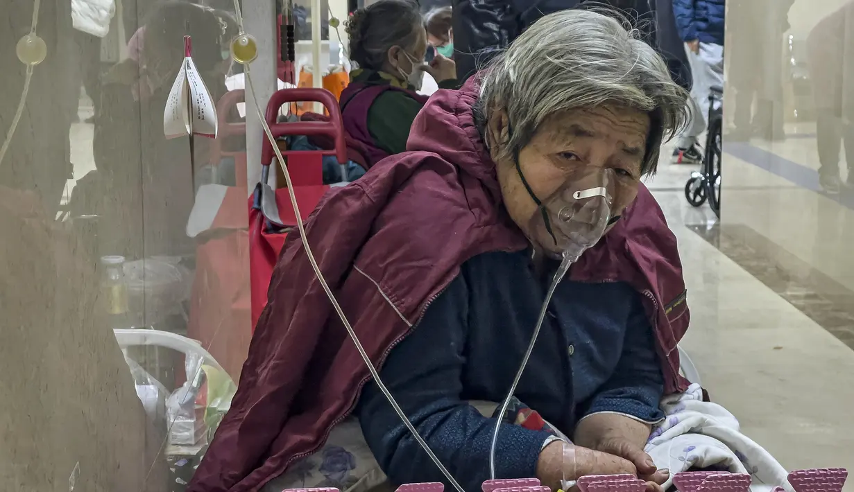 Seorang pasien lanjut usia (lansia) menerima infus saat menggunakan ventilator di lorong bangsal darurat di Beijing, Kamis (5/1/2023). Pasien, kebanyakan dari mereka lansia, berbaring di tandu di lorong dan menerima oksigen sambil duduk di kursi roda saat kasus COVID-19 melonjak di ibu kota China, Beijing. (AP Photo/Andy Wong)