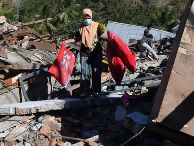 Seorang perempuan membawa bantal melalui puing-puing rumah yang rusak di Menggala, Lombok Utara, Rabu (8/8). Laporan terakhir mengatakan, gempa Lombok telah memakan 105 korban jiwa, dan lebih 70.000 orang kehilangan tempat tinggal. (AFP/ADEK BERRY)