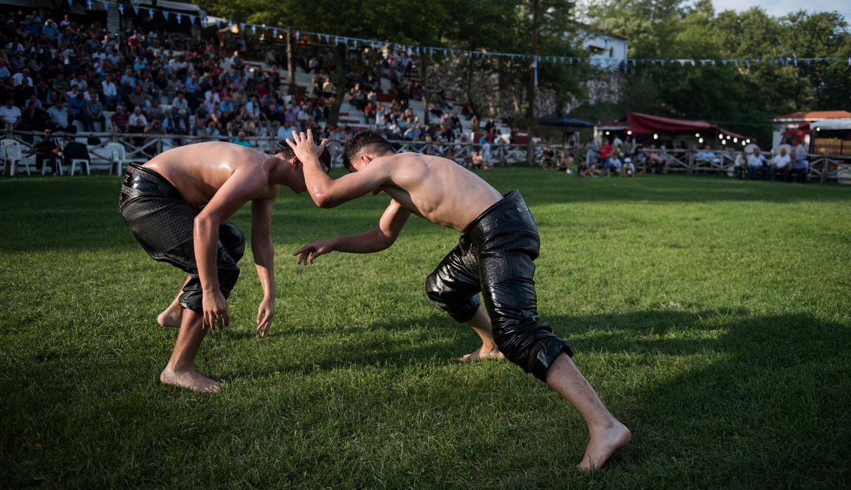 Dua pegulat sedang beraksi berusaha saling menjatuhkan dalam kompetisi tahunan gulat minyak tradisional di Sochos, Yunani, 30 Juni 2018. Lebih dari seratus drum minyak zaitun habis untuk melumuri sekujur tubuh setiap peserta. (AP/Giannis Papanikos)