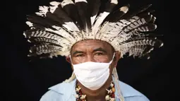 Pemimpin adat dari etnis Mura, Pedro dos Santos memakai pakaian tradisional dan masker saat pandemi virus corona COVID-19 di Taman Bangsa Adat, Manaus, Brasil, Kamis (28/5/2020). Pada bulan April, dos Santos, istri, anak-anak, dan cucunya jatuh sakit dengan gejala COVID-19. (AP Photo/Felipe Dana)
