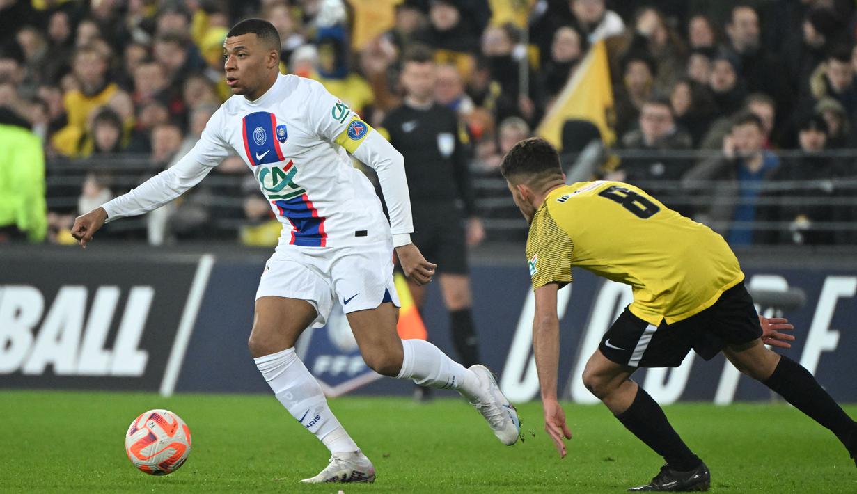 Pemain PSG, Kylian Mbappe (kiri) berusaha melewati pemain US Pays de Cassel, Clement Boudjema pada laga babak 32 besar Coupe de France 2022/2023 di Stade Bollaert-Delelis, Selasa (24/1/2023) dini hari WIB. Mbappe berhasil mencetak lima dari tujuh gol kemenangan Paris Saint-Germain. (AFP/Francois Lo Presti)