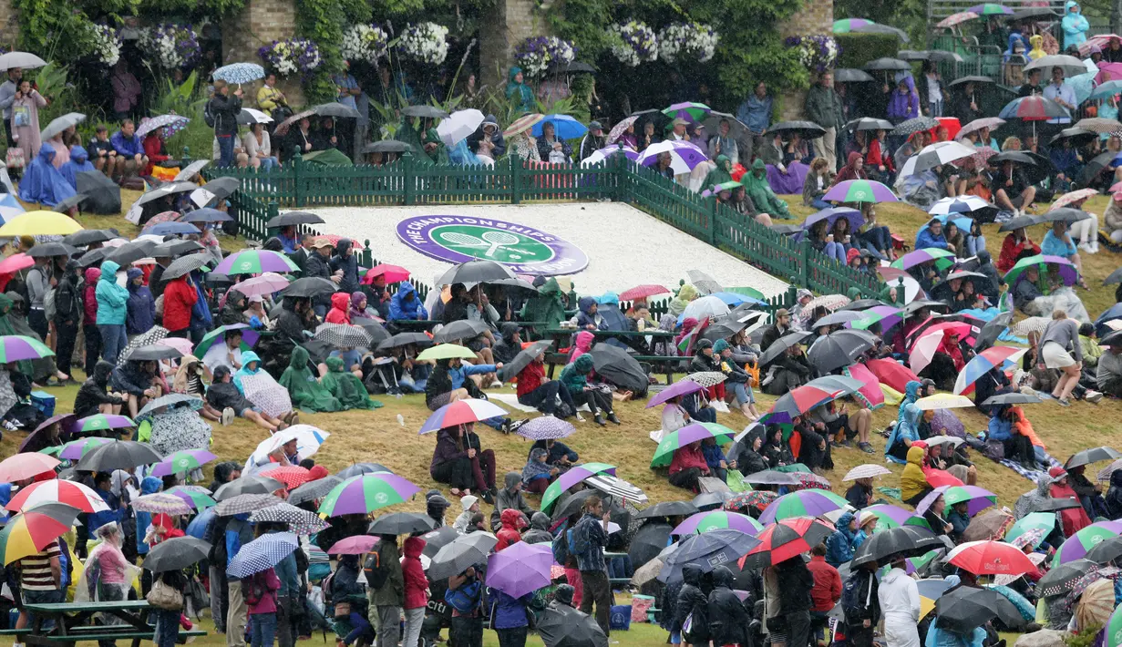 Para penonton memakai payung saat menyaksikan perempat final tunggal wanita antara Simona Halep asal Romania dan petenis Inggris Johanna Konta di sebuah layar lebar pada kejuaraan tenis Wimbledon 2017 di London (11/7). (AP Photo/Kirsty Wigglesworth)