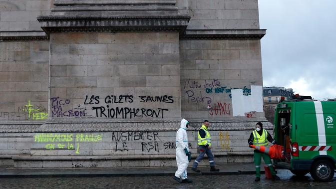 Pekerja membersihkan grafiti bertuliskan 'jaket kuning akan menang' di Arc de Triomphe, Paris, Prancis, Minggu (2/12). Kenaikan pajak bahan bakar memicu kerusuhan di Paris. (AP Photo/Thibault Camus)
