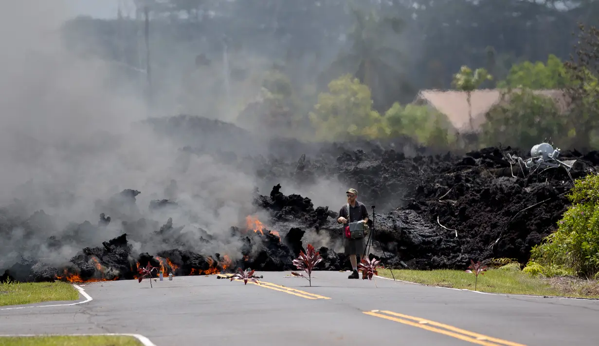 Seorang lelaki mengambil gambar lava pijar erupsi Gunung Kilauea yang menutupi jalan di Pahoa, Hawaii, Amerika Serikat, Sabtu (5/5). Aliran lava pijar membakar apa saja yang berada di sekitarnya. (AP Photo/Marco Garcia)