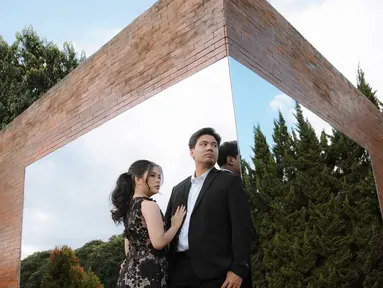Dalam pemotretan bertema dramatis, mereka menghadirkan konsep yang lebih elegan dan berkelas. Indah tampil memukau dalam gaun hitam beraksen renda dengan rambut yang ditata rapi, sedangkan Frans memilih setelan jas hitam yang membuatnya terlihat berwibawa. Latar dinding bata dan cermin besar berpadu dengan refleksi langit biru, menciptakan hasil foto yang artistik dan memanjakan mata.  (Liputan6.com/IG/@fransfaisal_)