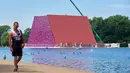 Pria berjalan di dekat pembangunan 'The Mastaba', sebuah karya luar ruangan yang terdiri dari lebih dari 7.000 tumpukan tong oleh seniman Bulgaria Christo Vladimirov Javachef di danau Serpentine di Hyde Park di London (11/6). (AFP Photo/Niklas Hallen)