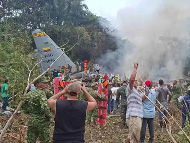 Orang-orang berdiri di sekitar pesawat kargo militer yang jatuh setelah lepas landas dari Puerto Leguizamo, Kolombia, sebuah kotamadya terpencil di provinsi Amazon Putumayo, Senin, 23 Maret 2026. Sebuah pesawat angkut militer milik Angkatan Udara Kolombia jatuh saat lepas landas di wilayah selatan Provinsi Putumayo. (MiPutumayo via AP)