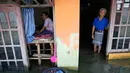 Sudarto berdiri di depan pintu rumahnya yang terendam banjir saat putrinya Turiah memandangi rumah mereka yang terendam banjir di Timbulsloko, Jawa Tengah, Indonesia, 31 Juli 2022. Dengan keterbatasan fisik yang menghalangi Turiah dari pekerjaan normal di desa, ia menghabiskan harinya dengan duduk di jendela depan rumah di atas panggung kayu yang ditinggikan. (AP Photo/Dita Alangkara)