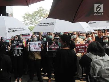 Pegawai KPK membawa poster saat menggelar aksi di Lobi Gedung KPK, Kuningan, Jakarta, Jumat (6/9/2019). Dalam aksi menolak revisi UU KPK tersebut, mereka mengenakan baju serba hitam lengkap dengan masker penutup mulut dan memasang KPK Lines di sekitar pintu masuk. (merdeka.com/Dwi Narwoko)