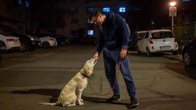 Iulian Barbulescu (34) berpose dengan anjingnya Jesse  (5 bulan) di Bucharest (28/3/2020). Undang-undang militer, yang disahkan pemerintah Rumania untuk mengurangi penyebaran virus corona, menyatakan berjalan bersama anjing adalah salah satu  kegiatan yang masih diizinkan. (AFP/Andrei Pungovschi)